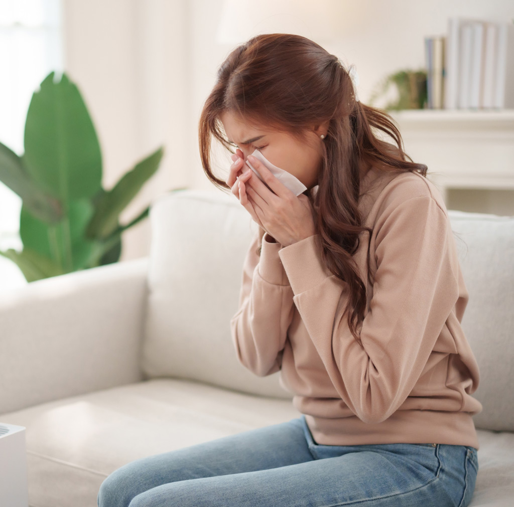 Woman with allergies blowing her nose into tissue 2